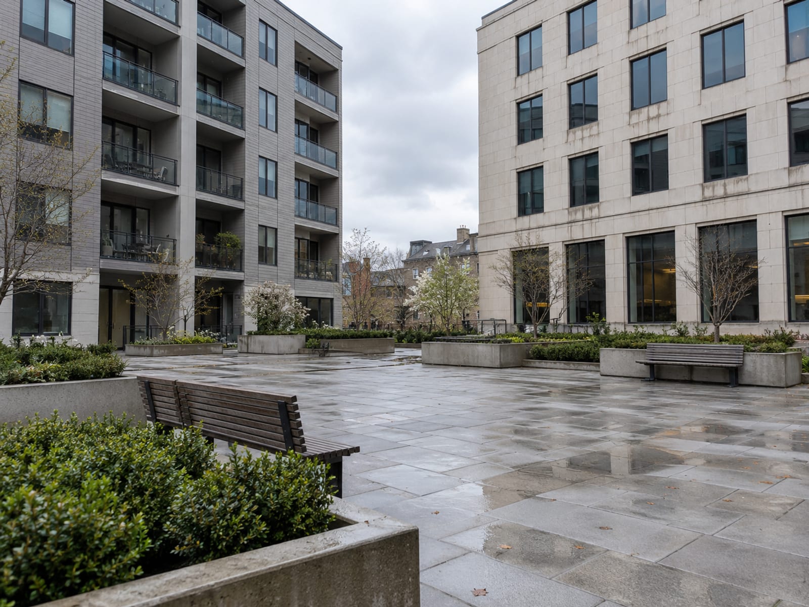 A mid-rise apartment building and a neighboring office block seen across an empty plaza on an overcast day