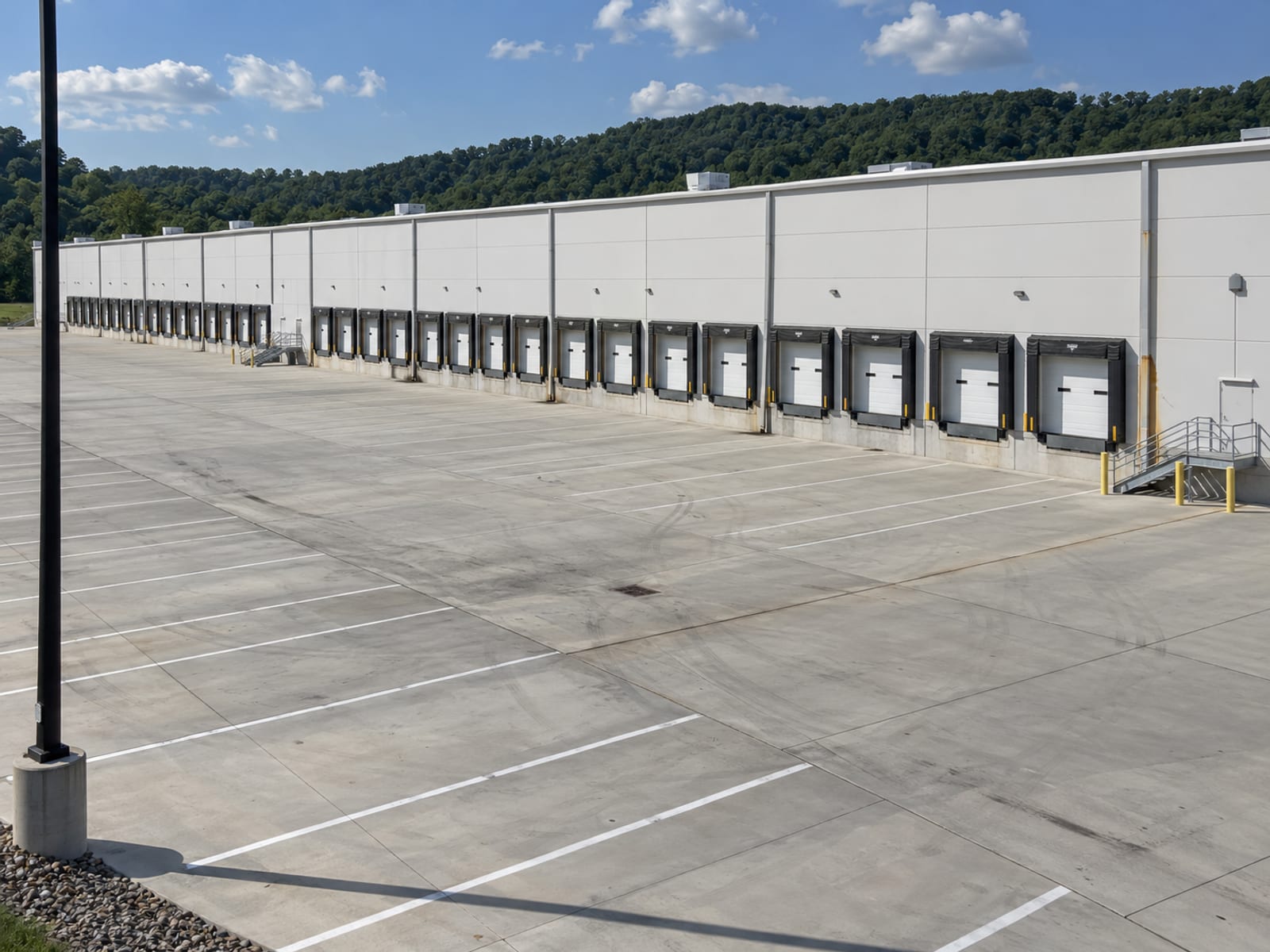 Una gran bodega de distribución de un solo piso con las puertas de los muelles cerradas y un patio de camiones vacío a la luz del día