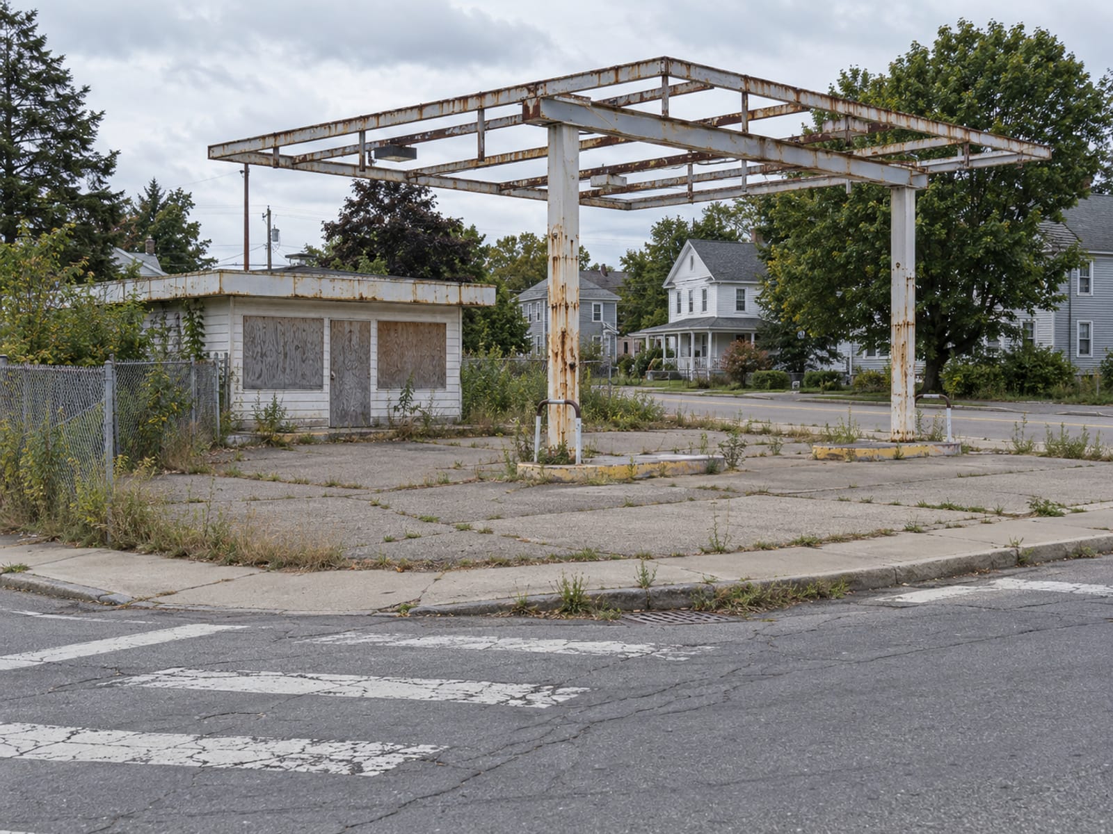 Un terreno de esquina vacío de una antigua estación de servicio con la estructura de un techo vacía y maleza en el pavimento
