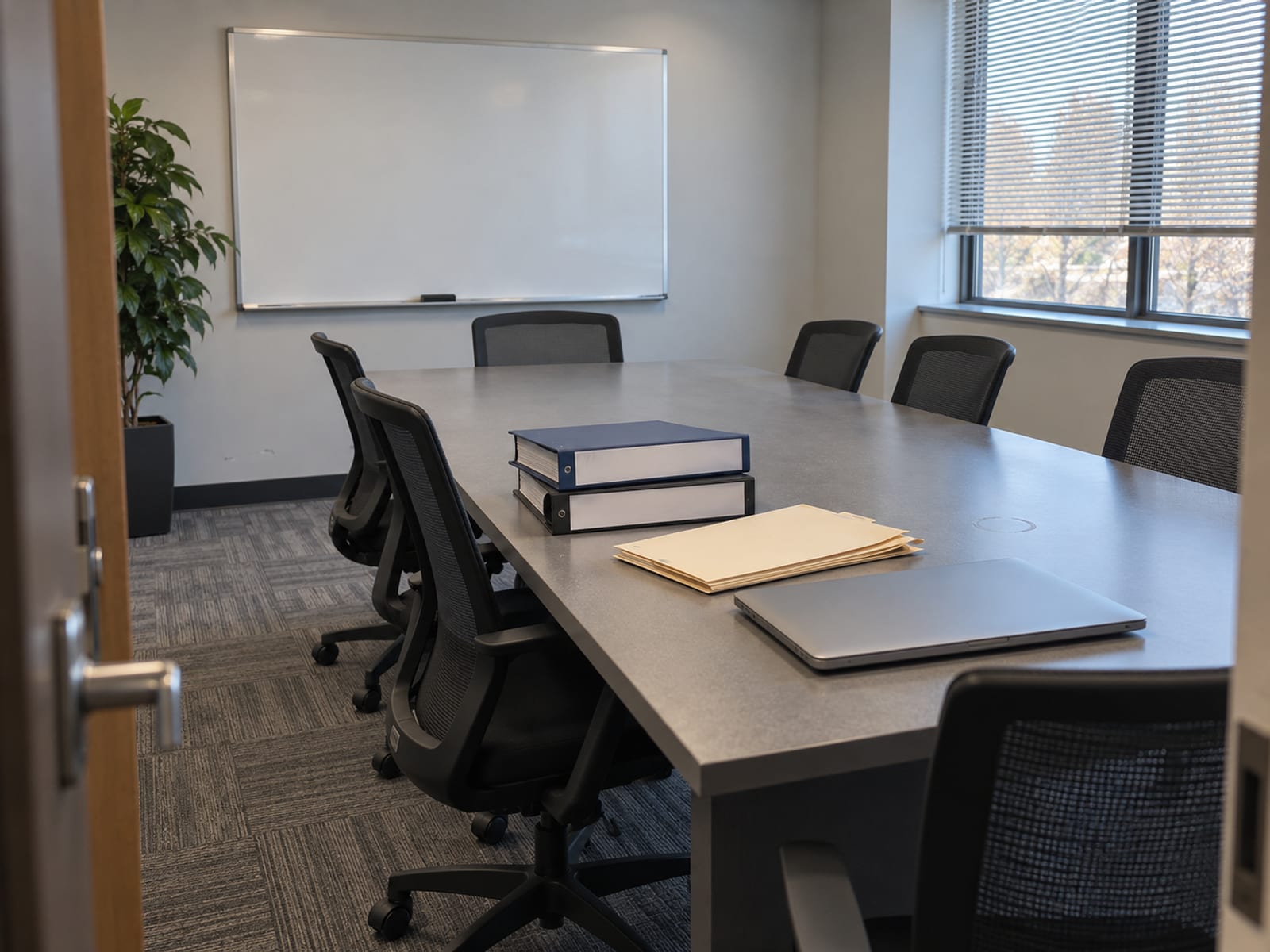 Binders, folders and a closed laptop on a conference table in an empty meeting room