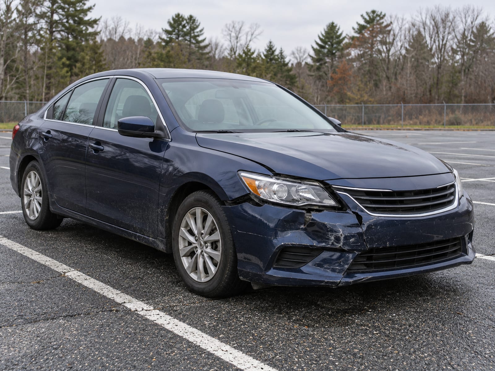 A sedan with a crumpled front bumper parked in an empty lot