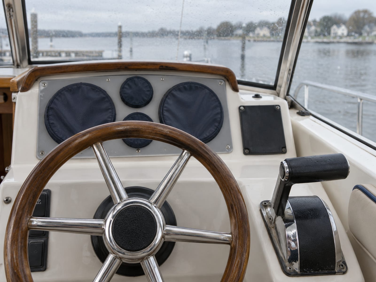 A recreational boat's helm with a steering wheel and covered instruments seen from the cockpit