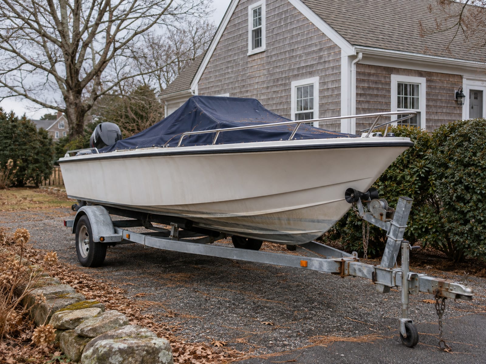 A small motorboat on a trailer in a residential driveway beside a garage on a sunny day