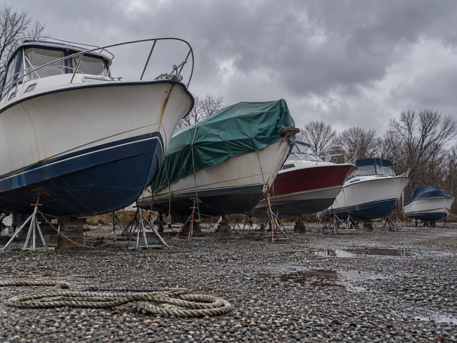 Boats hauled out of the water and resting on stands in a boatyard under a gray sky