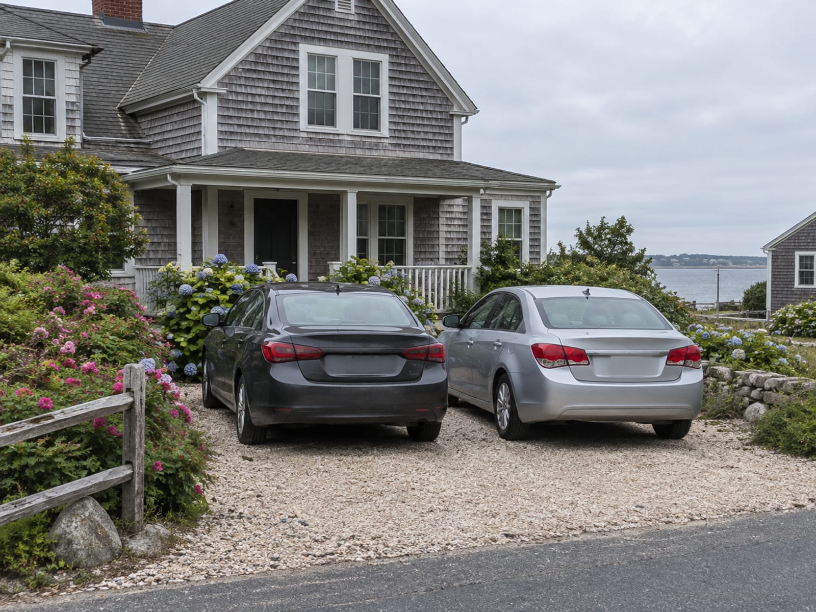 Two cars parked side by side in the driveway of a shingled Rhode Island home