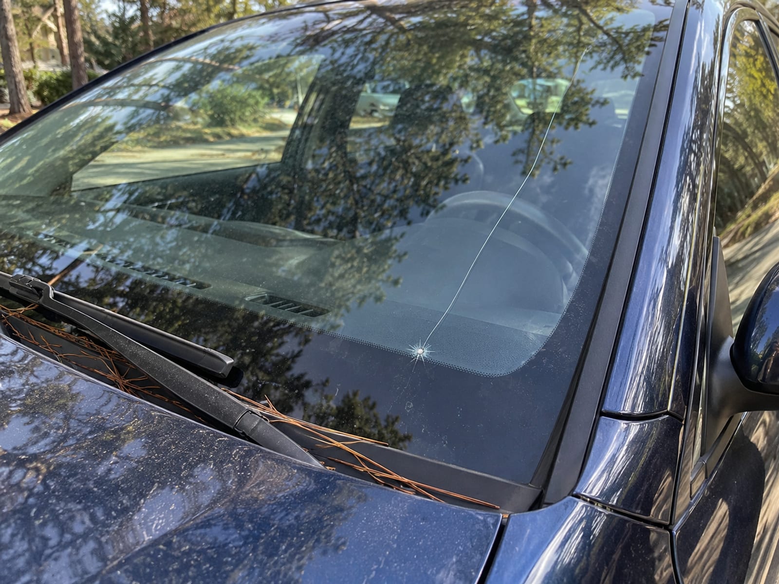 Un parabrisas agrietado en un auto estacionado, visto desde afuera a la luz del día