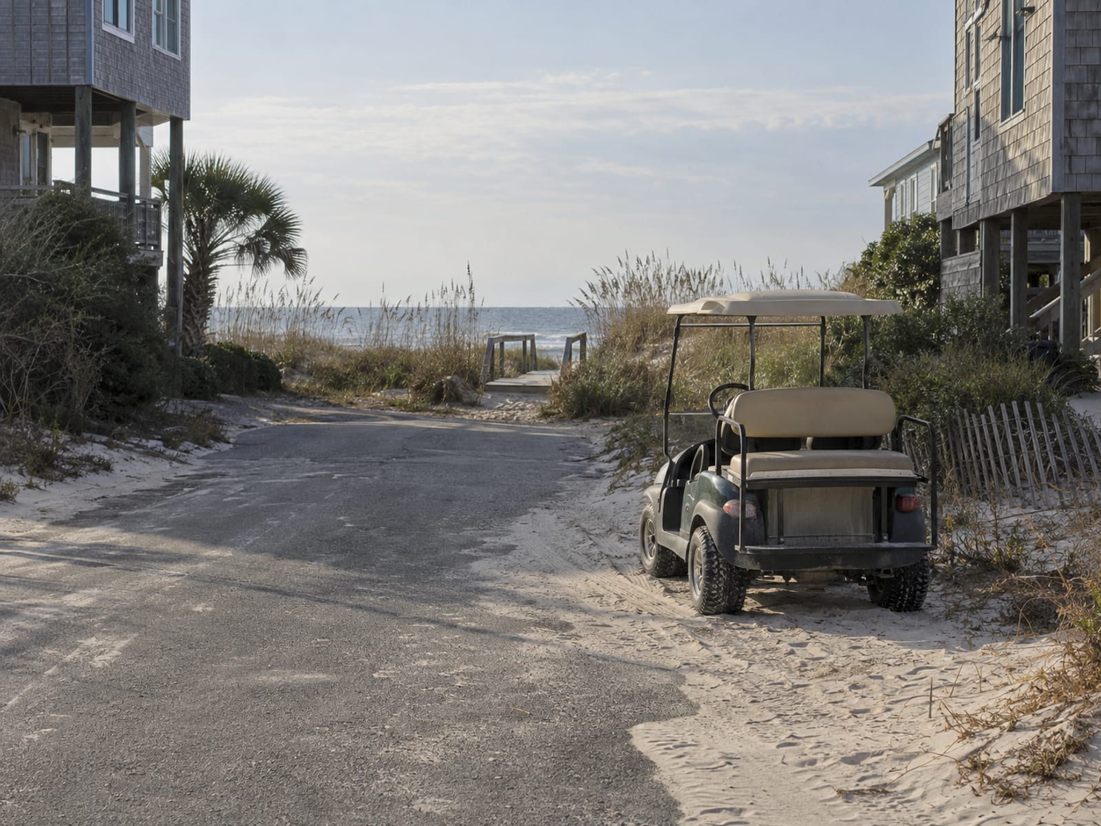 An empty golf cart parked at the end of a quiet beach town street near sea oats and dunes in low winter light