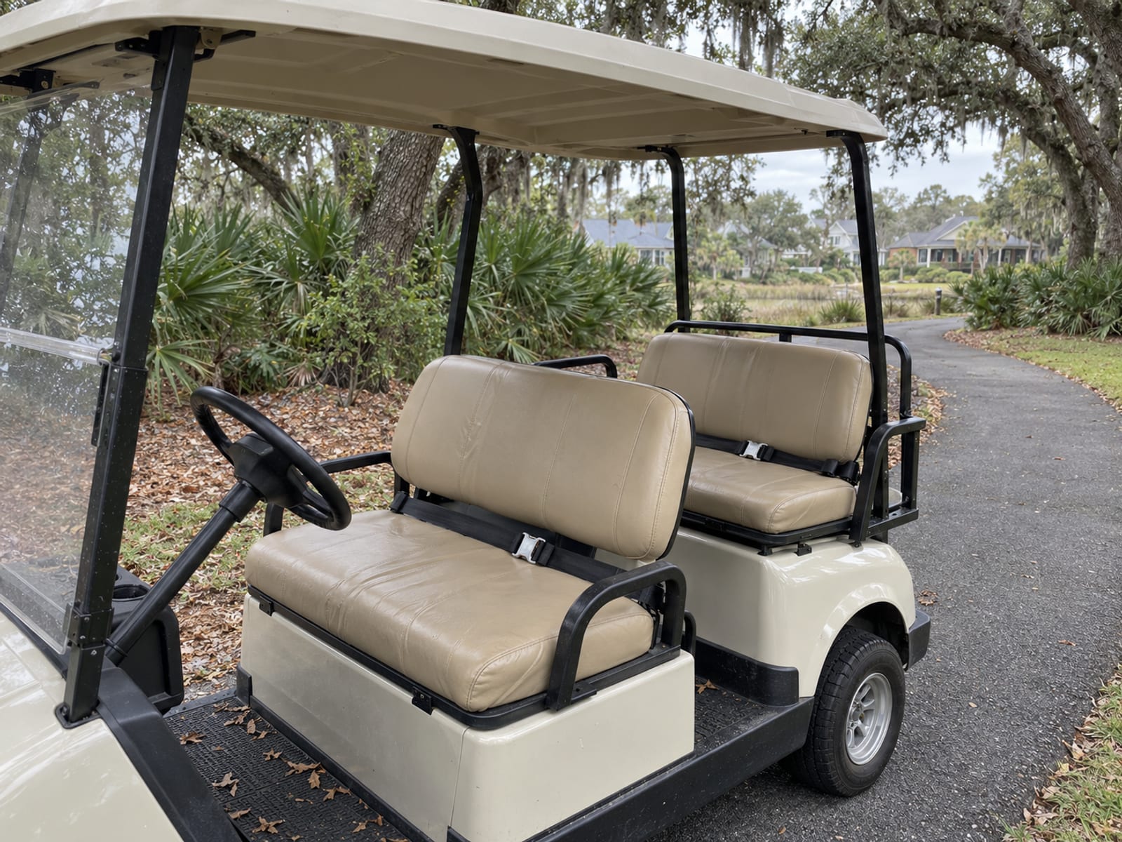 A golf cart with seat belts fitted on both rows of seats parked on a neighborhood path