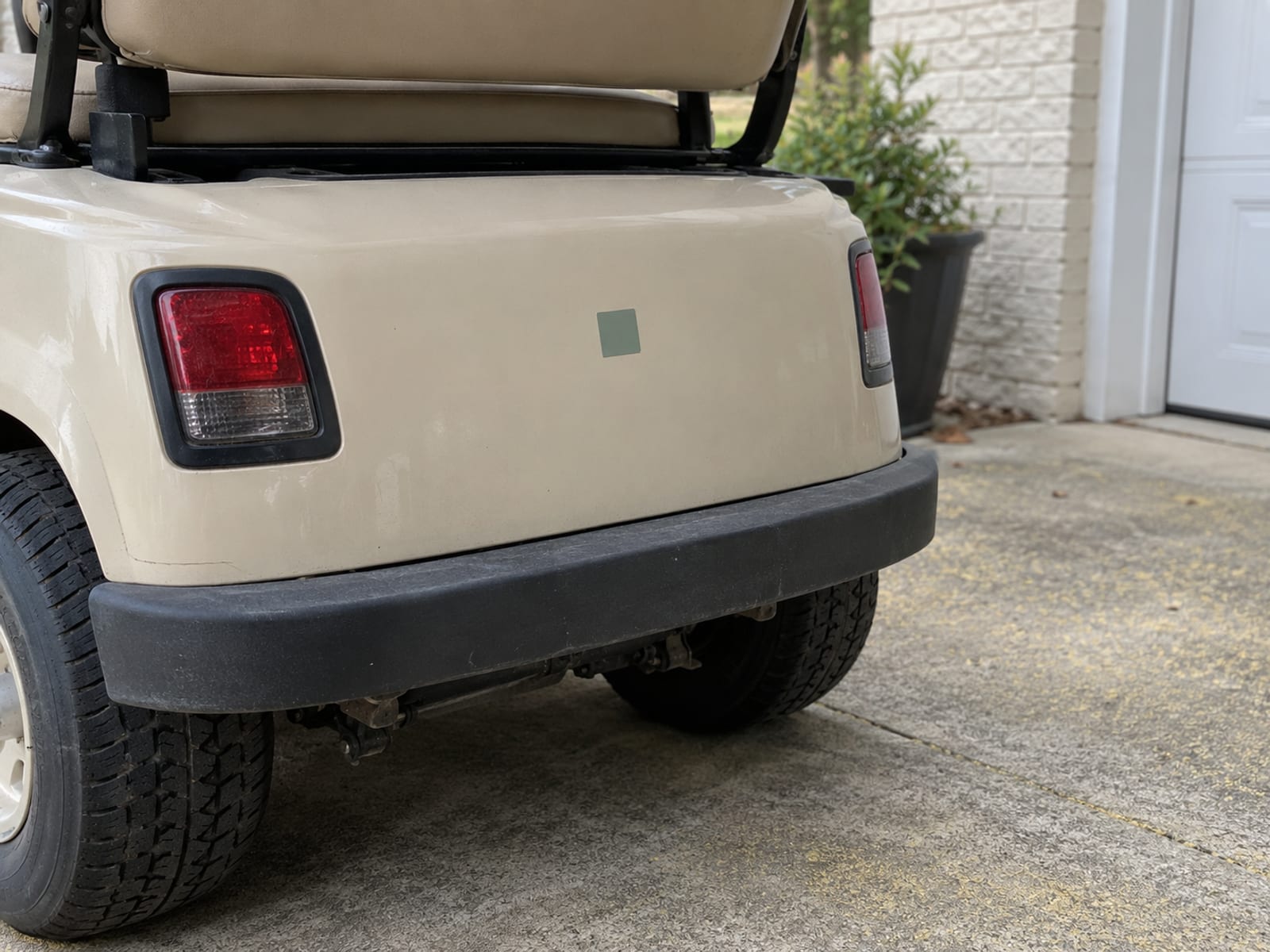 A golf cart parked in a home driveway with a permit decal on its rear panel