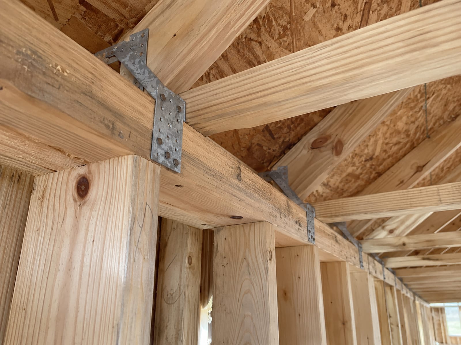 Metal hurricane straps fastening wooden roof trusses to the top of a house wall