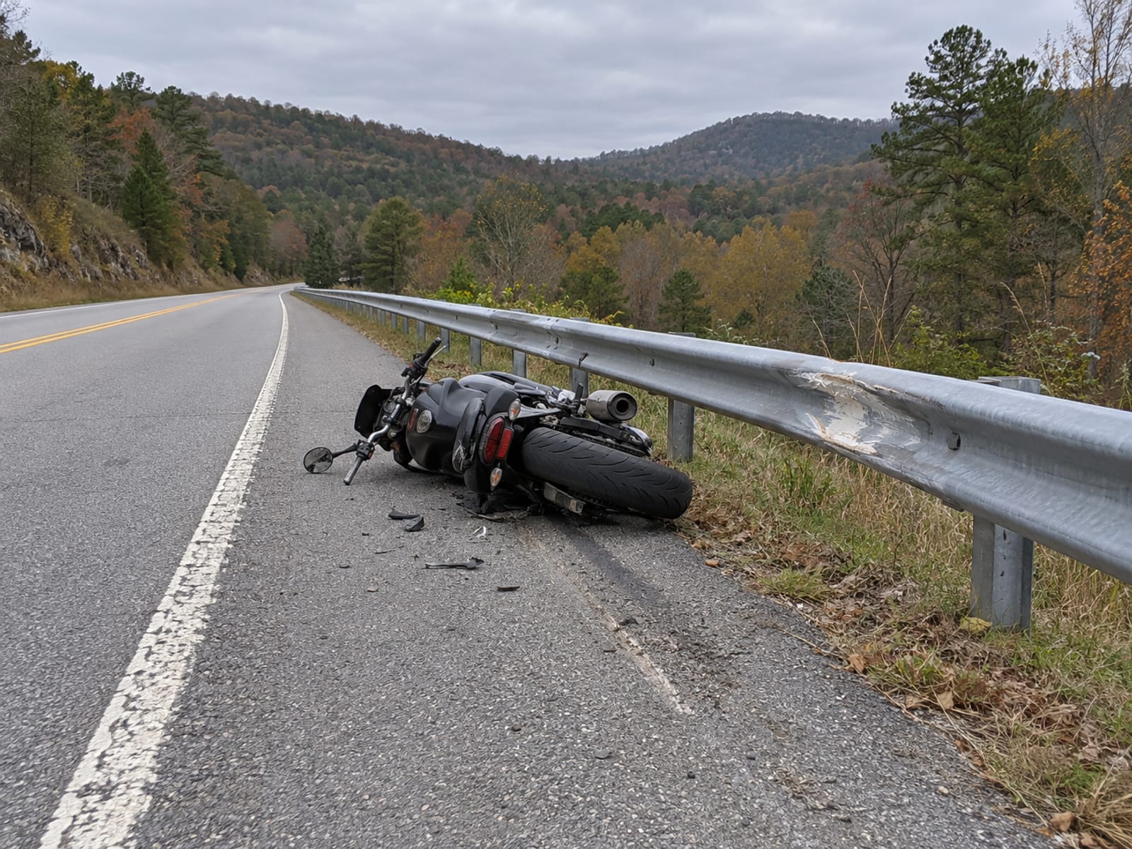 A motorcycle lying on its side on a road shoulder beside a scraped guardrail