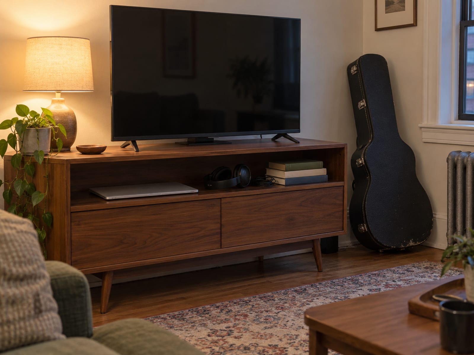 A living room shelf holding a television, a laptop, headphones and a guitar case