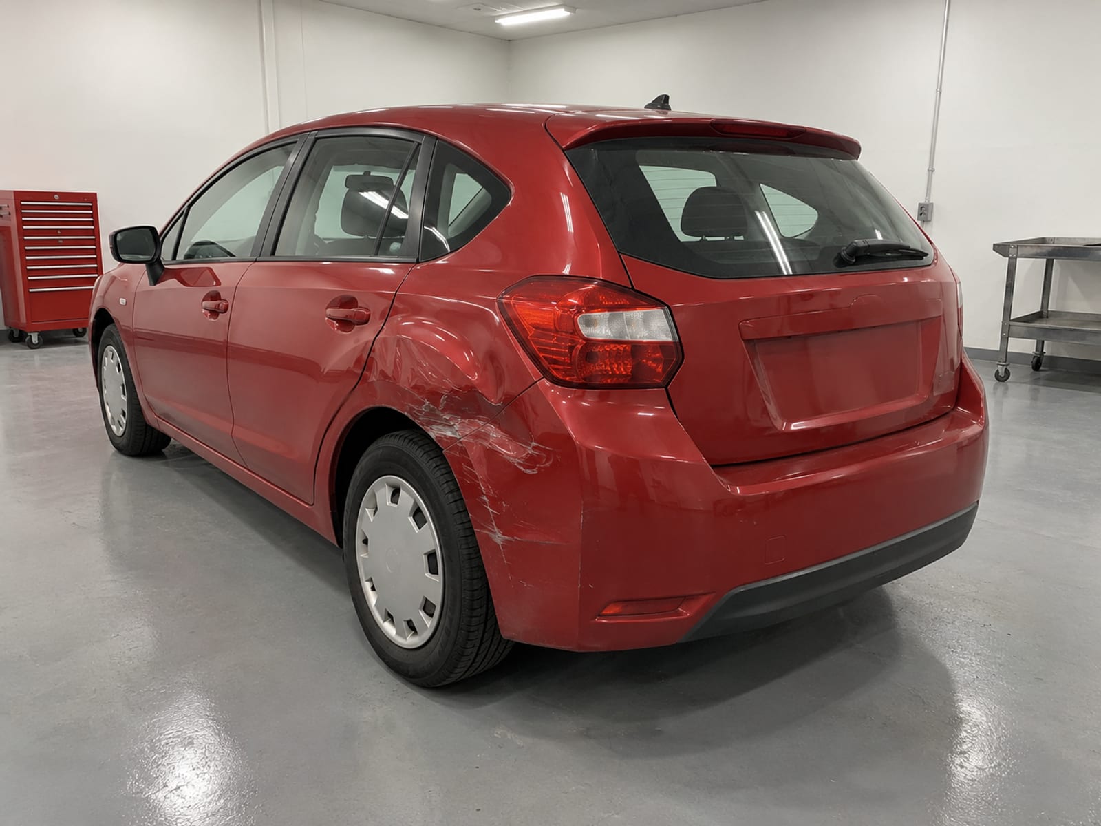 A car with a crumpled rear quarter panel parked in a repair shop bay