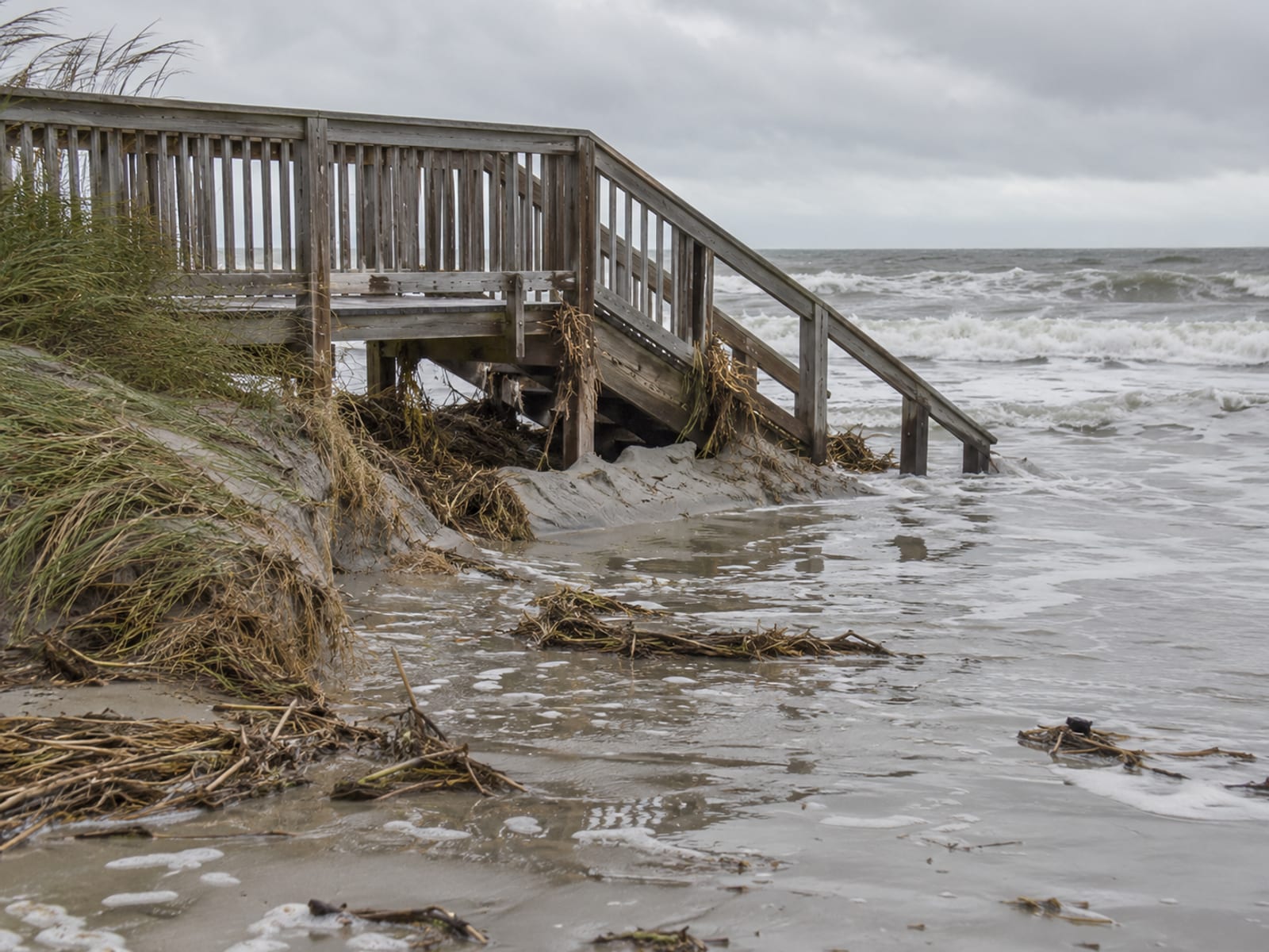 A wooden dune walkover partly covered by high water and sand after a coastal storm