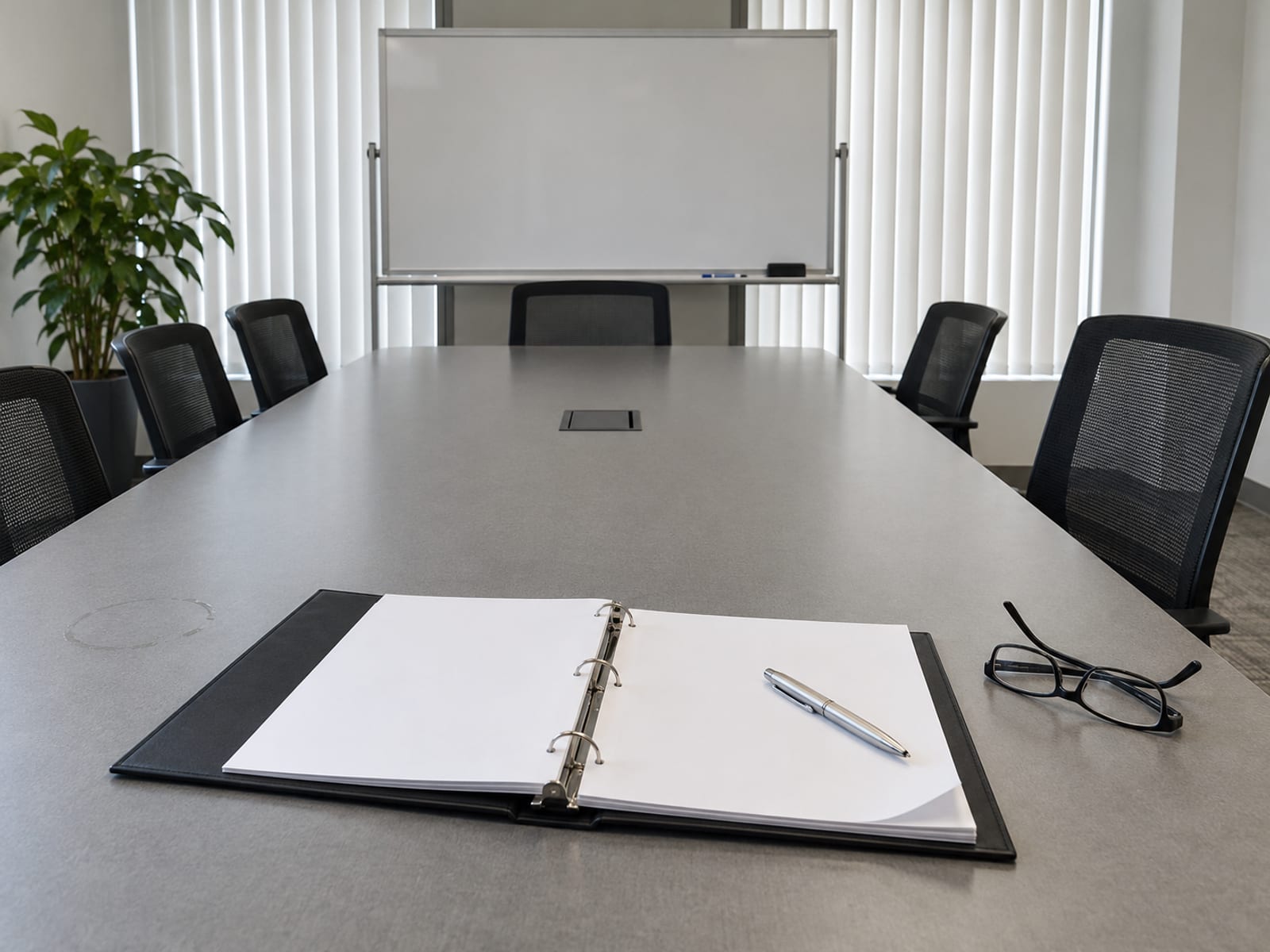 A conference table with an open binder, a pen and a pair of reading glasses