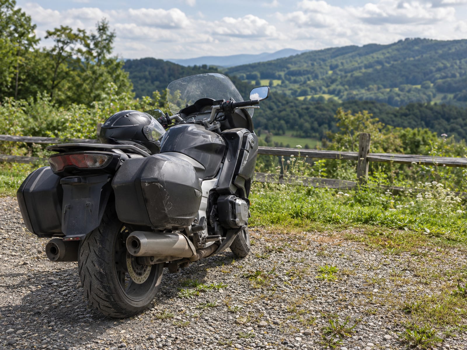 A touring motorcycle with saddlebags and a helmet resting on the seat, parked on a gravel overlook