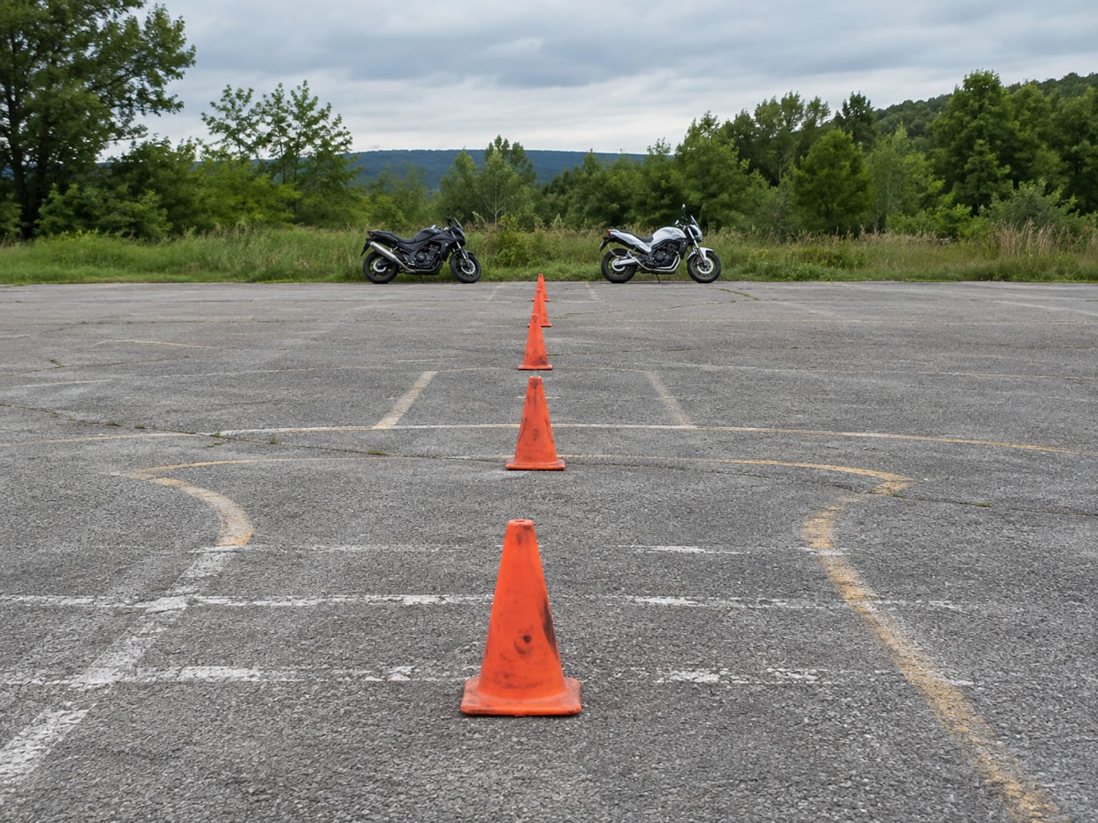 Two motorcycles parked on an empty paved lot marked with orange traffic cones