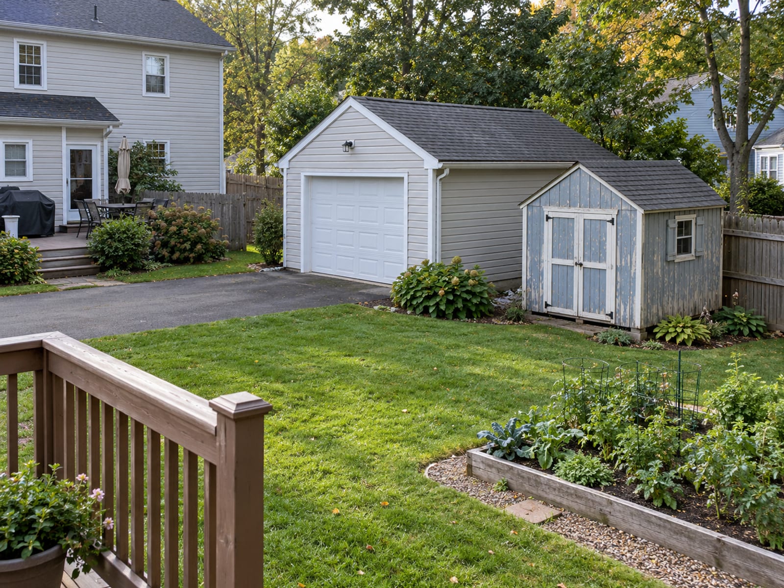 A detached garage and a garden shed behind a two-story house with a fenced backyard