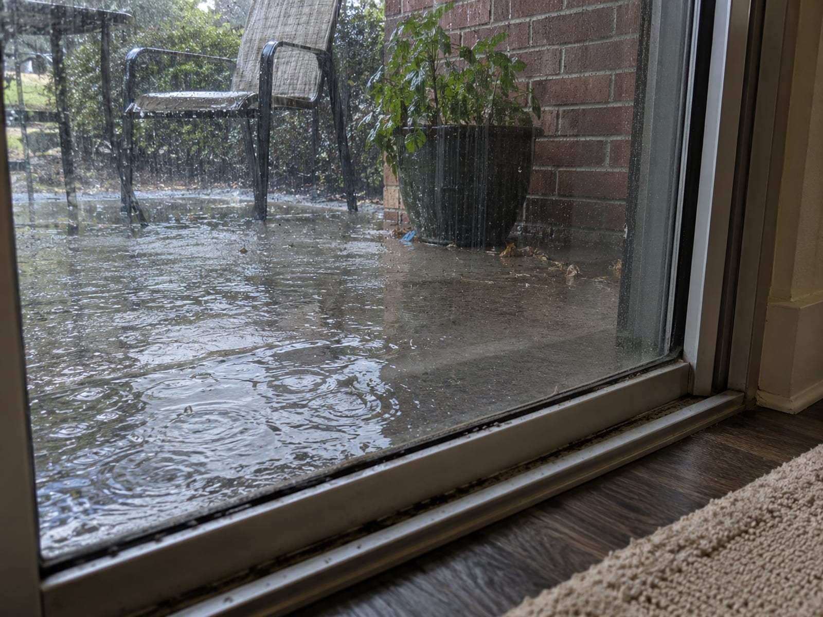 Lluvia fuerte acumulada en el patio de un apartamento de planta baja junto a una puerta corrediza de vidrio