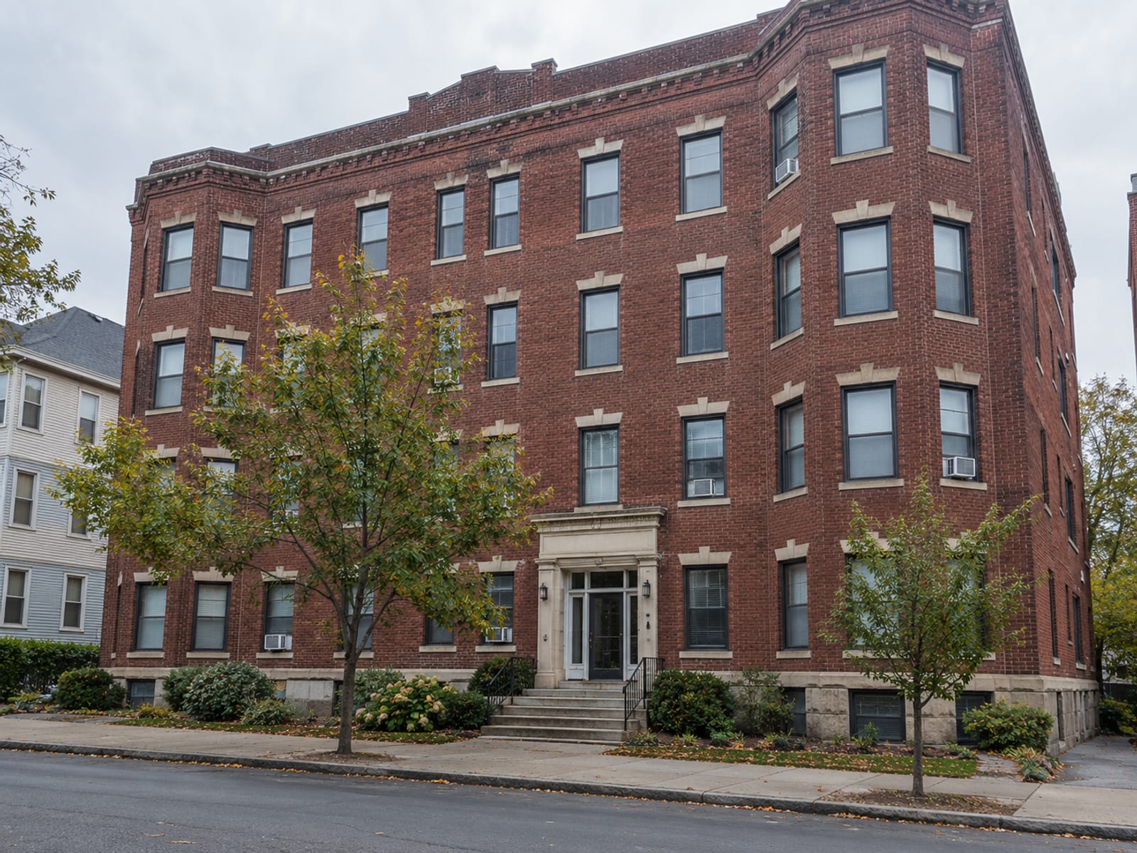 A brick apartment building with rows of windows on a quiet street, no readable signage