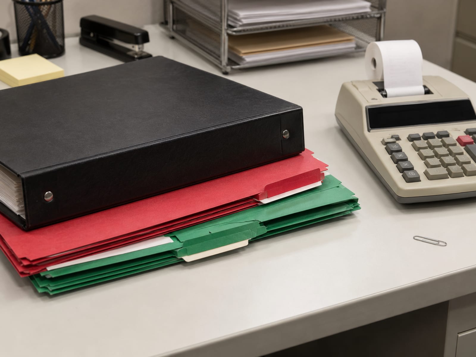 A tidy desk with stacked payroll folders, a calculator and a closed binder under office light